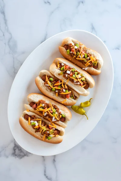 Overhead view of a plate of chili dogs on a white marble counter.