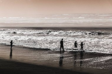 Sahilde gün batımında çocuklarla çevrili bir adamın silueti.