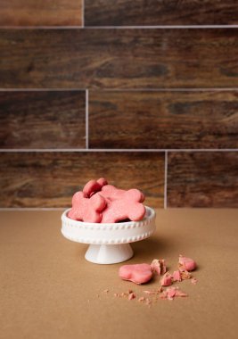 Pembe köpek beyaz kek tezgahında kahverengi ahşap arka planda duruyor.