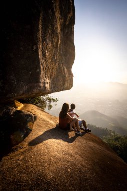 Kayalık kenardaki çift güzel dağdan gün batımını izliyor.