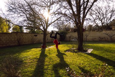 Gün batımına karşı iki ağaç arasında yoga yapan kadın.