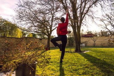 Gün batımına karşı iki ağaç arasında yoga yapan kadın.