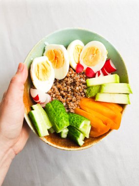 Haşlanmış yumurta, sebze ve Buckweata dolu bir kaseyi tutan kadının eli. 