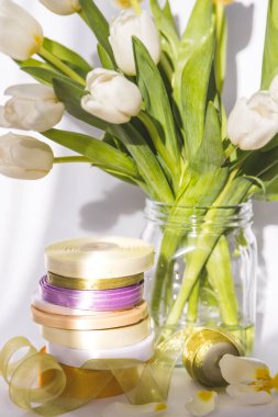 Vazodaki laleler, kurdeleler, iplikler, makas, beyaz arkaplandaki dikiş sepetleri.