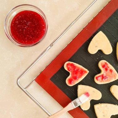 Siyah silikon paspasın üzerinde kırmızı reçelli kalp şeklinde kurabiyeler vardı.