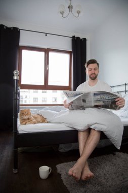 Genç adam gazete okuyor ve yatakta kahve içiyor, gerçek hayatta, kedi i