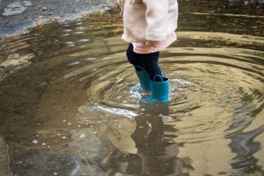 Lastik çizmeli bir kızın su birikintisinde duruş görüntüsü.