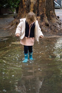 Lastik çizmeli bir kızın su birikintisinde duruşu.