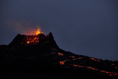 Sert kayalık volkan, gece gökyüzünün arka planında sıcak erimiş lav püskürtüyor.