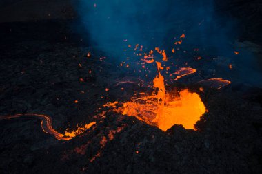 Aktif volkanın volkanik patlamasını, parlak turuncu lavların karanlık gecede sert yamaçlarda akışını.