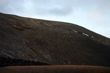 Dağlık arazide bulutlu gökyüzünün altında engebeli dağlara karşı duran uzak bir yürüyüşçü.