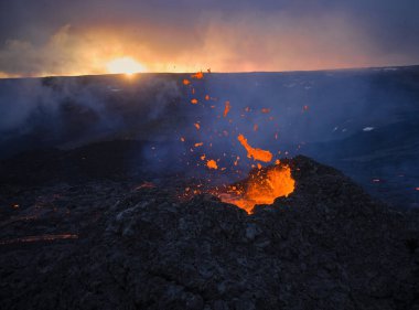 Yanan sıcak lav ve buharın gün batımında dağlık arazide aktif bir volkan kraterinden yayılması dramatik bir manzara.