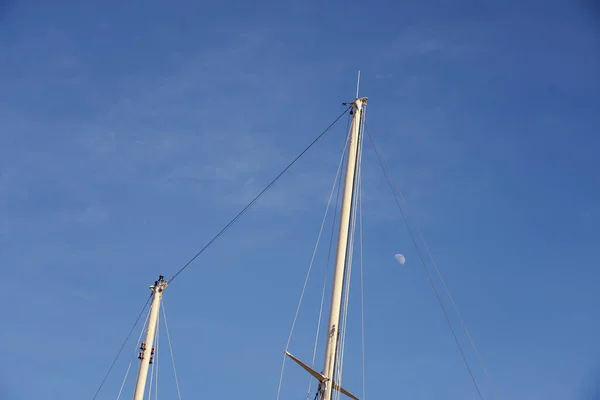 The yacht\'s masts against the blue sky with the moon with space for text.