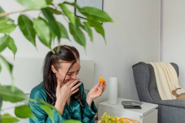 İpek pijamalı genç bir kadın yatakta yatarken sağlıklı kahvaltı yapar. Ev refahı kavramı. Genç bir kadının duygusal sağlığı