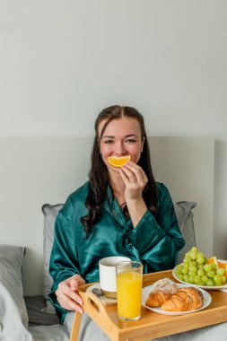 Genç bir kadın gülüyor ve ağzında bir portakal tutuyor. Ev konfor bölgesi ve sağlık konsepti.