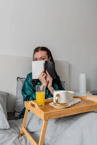 Молода Жінка Шовковій Піжамі Має Здоровий Сніданок Читає Книгу Лежачи — стокове фото