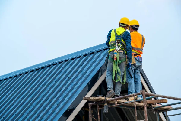 Roofer worker in protective uniform wear and gloves,Roofing tools,installing new roofs under construction,Electric drill used on new roofs with metal sheet.