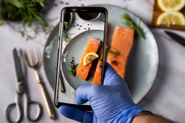 Eldivenli bir adam masada yemek fotoğrafı çekiyor.