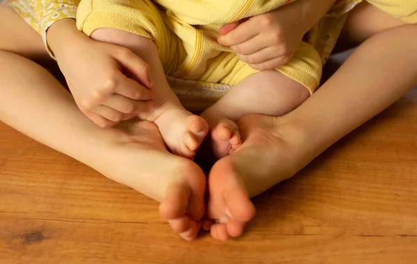 Two sisters sit at wooden floor, baby feet toes of two small girls