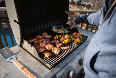 Man grilling chicken and vegetables outdoors on a gas bbq grill. clipart