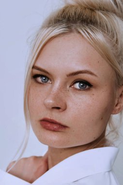 Beyaz duvarda güzel, genç, gülümseyen, zeki, sarışın çilli bir kadın. Beyaz gömlek giyen güzel bir kadın. Dost canlısı bir portre..
