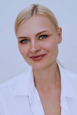 Beyaz duvarda güzel, genç, gülümseyen, zeki, sarışın çilli bir kadın. Beyaz gömlek giyen güzel bir kadın. Dost canlısı bir portre..