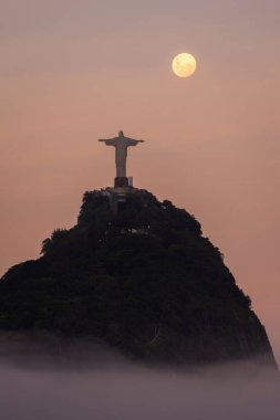 Corcovado Dağı 'nın güzel manzarası, Kurtarıcı İsa Heykeli ve gün batımında yükselen dolunay Rio de Janeiro, Brezilya' daki yağmur ormanları dağ parkından görülüyor.