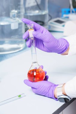 Araştırmacı elinde kimyasallar ve reaktörlerle dolu bir şişe tutuyor.