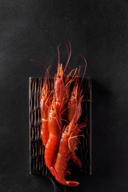 Ahşap servis tahtasındaki kırmızı karideslerin üst görüntüsü. Siyah arka planda, kopyalanmış. Dikey resim