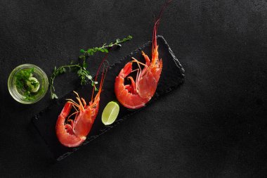 İki kaynamış kaplan karidesinin üst görüntüsü kireç, taze otlar ve sarımsak sosuyla servis ediliyor.