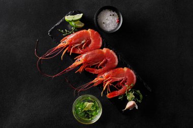 Deniz ürünleri lezzetleri. Buharda pişmiş karideslerin üst görüntüsü siyah tahtada servis edilir baharatlar, limon dilimleri ve sarımsak sosuyla birlikte.