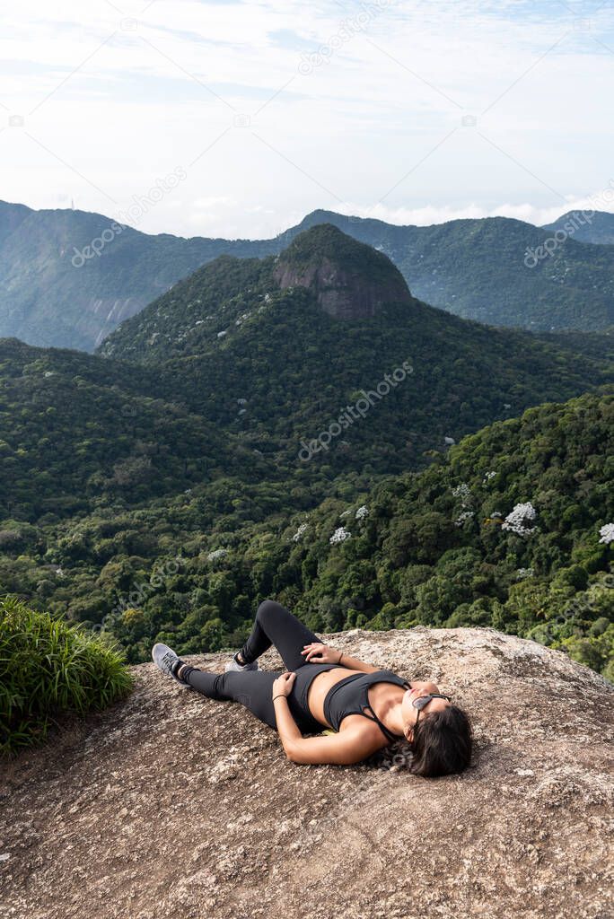 Beautiful view to woman laying down and resting on rocky rainforest mountain top, Tijuca Park, Rio de Janeiro, Brazil
