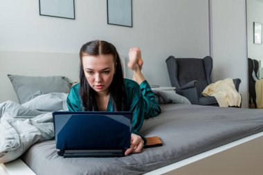 Genç kadın yatak odasında yatarken dizüstü bilgisayarda çalışıyor. Uzaktan kumanda kavramı. Sağlık ve ruh sağlığı kavramı