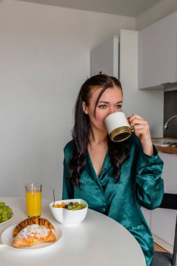 Genç bayan ipek pijama kahvaltı yapar ve evdeki mutfakta kahve içer. Refah kavramı.
