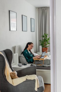 Genç kadın yatak odasında yatarken dizüstü bilgisayarda çalışıyor. Uzaktan kumanda kavramı. Sağlık ve ruh sağlığı kavramı