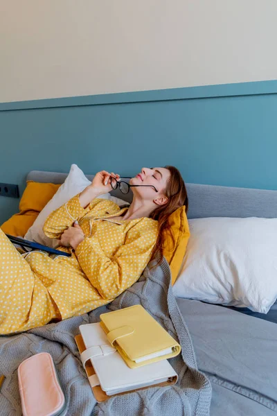 穿着舒适的黄色睡衣的年轻女人躺在卧室的床上工作 女商人做着远离社会的工作 新的正常概念 — 图库照片