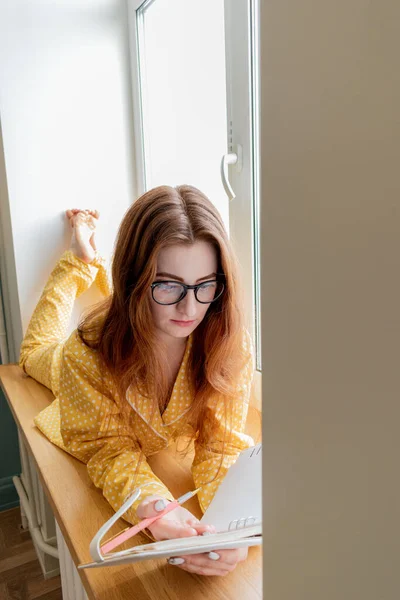 Молода Жінка Зручній Жовтій Піжамі Працює Лежачи Підвіконні Спальні Ділова — стокове фото