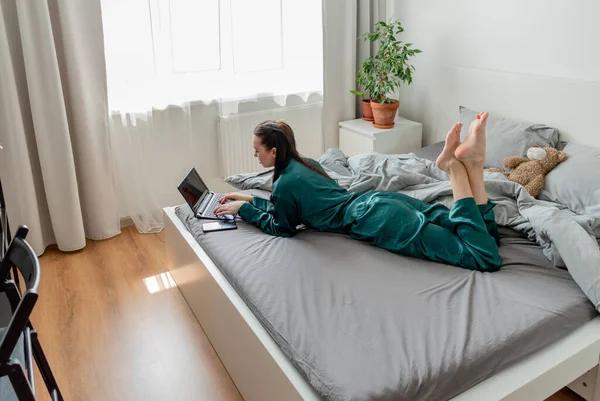 Genç kadın yatak odasında yatarken dizüstü bilgisayarda çalışıyor. Uzaktan kumanda kavramı. Sağlık ve ruh sağlığı kavramı