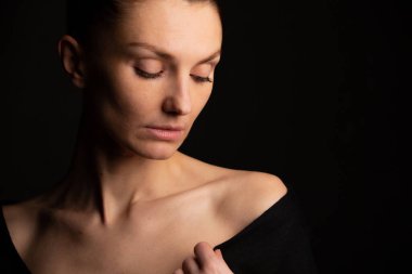 Siyah arka planda omuzları açık bir kızın portresi.