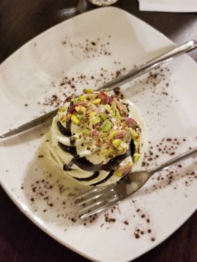 Beyaz bir tabakta çatal ve kaşığın yanında fıstıklı dondurma.