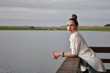 Gölün kıyısında kara kara düşünen güzel bir kadının portresi.