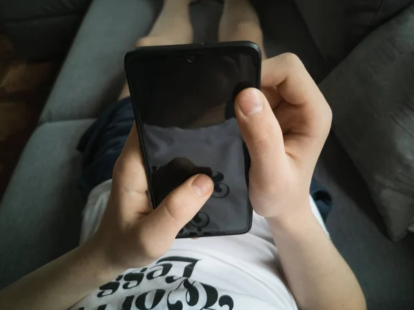 Boy 13-15 years old on the couch with a smartphone in his hands