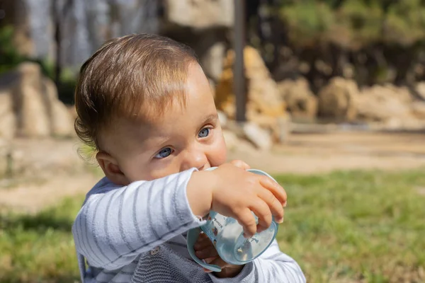 Güneşli güzel bir günde, İspanya 'da bir parkta açık havada oynayan küçük bir oğlan çocuğu. O, su şişesini içiyor. Kafkasyalı ve mavi gözleri var. O gri ve gökyüzü mavisi bir kazak giyiyor. O yalnız ve eğleniyor..