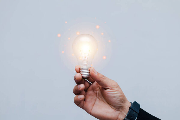 Business man hand with glowing incandescent lamp on dark white background.