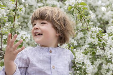 Bahçede açan beyaz çiçeklerin arasında gülümseyen bir çocuk.