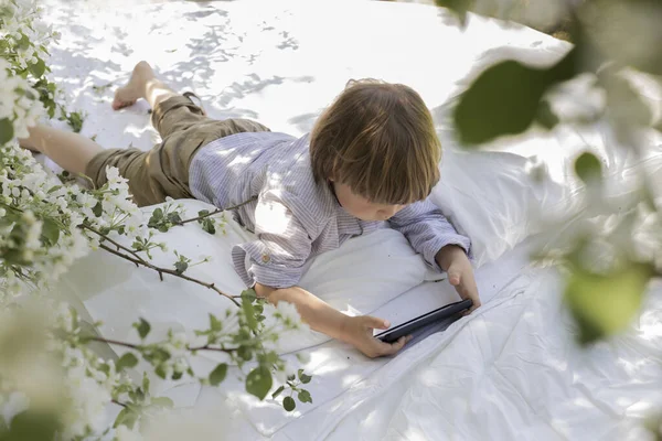 Top view of child playing in gadget and laying in bed in the garden
