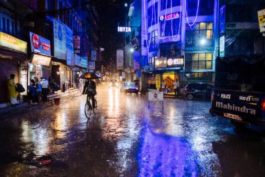Nepalli adam, gece vakti Nepal 'de şiddetli muson yağmurları sırasında Thamel' in ana caddelerinde bisiklet sürüyor..