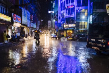 Nepali man cycling in Kathmandu main streets of Thamel during heavy monsoon rain at night time in Nepal. clipart
