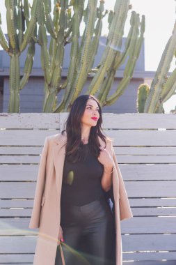 Güzel esmer kadın ceketini tutuyor ve kameradan kafasını çeviriyor.