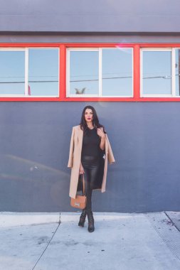 Gri duvarın önünde duran iş kadını, turuncu pencereler.